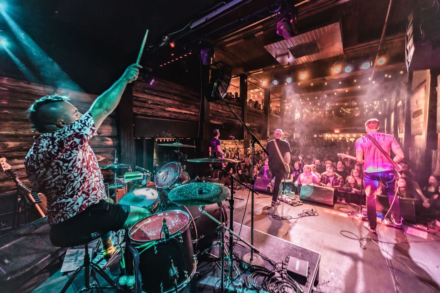 Dynamic concert scene with drummer and performers on colorfully lit stage during live show.