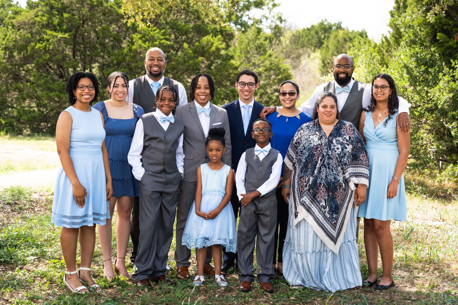 Extended family portrait with members wearing coordinated blue and white formal attire outdoors.