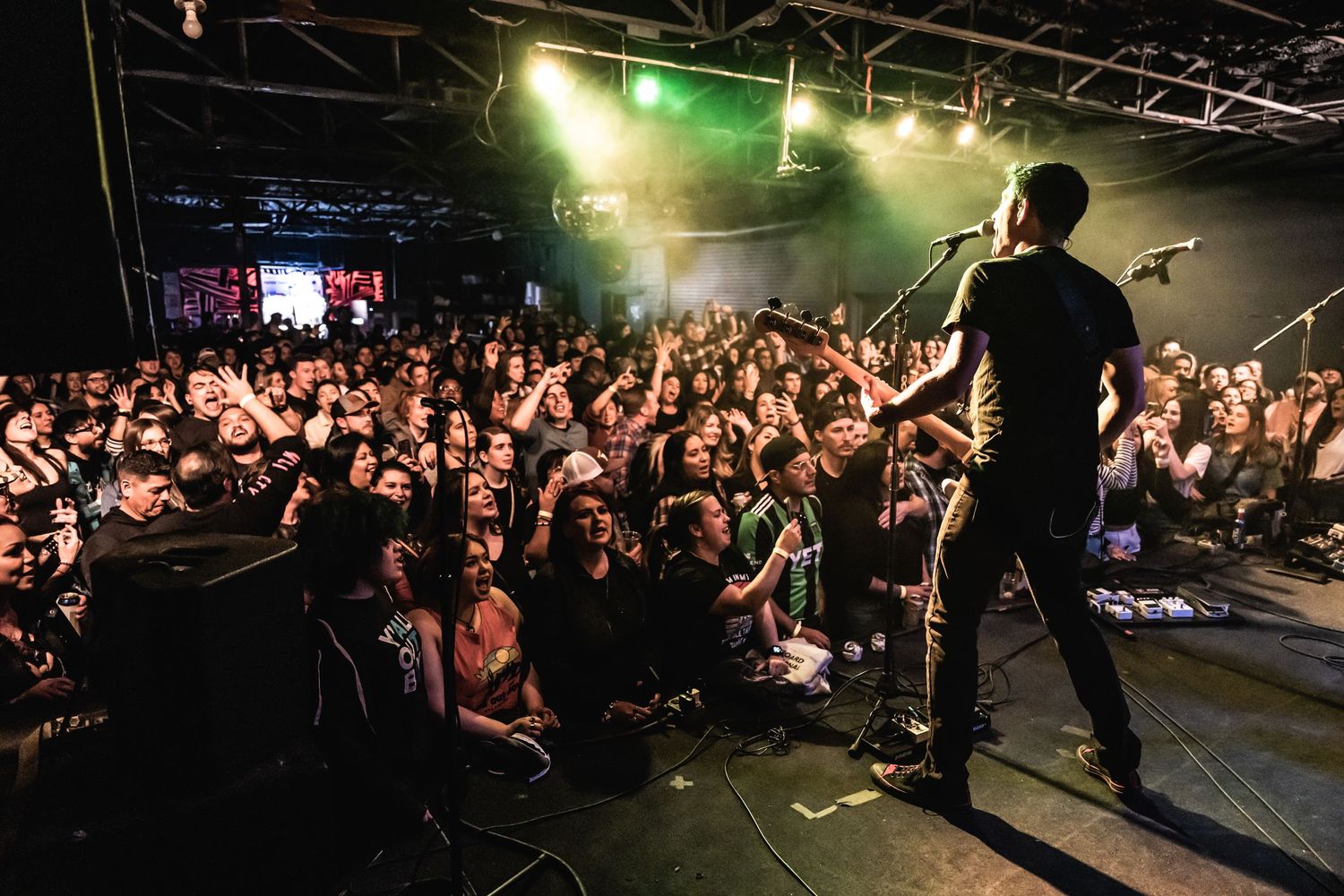 A silhouetted performer stands on stage facing a packed crowd during a live show.