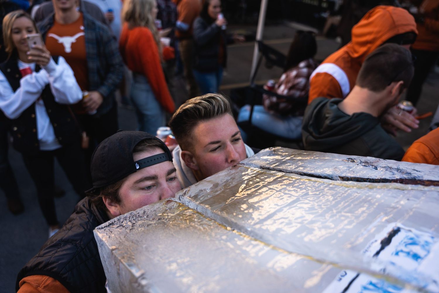 People lean over to drink from an ice luge at an outdoor event.