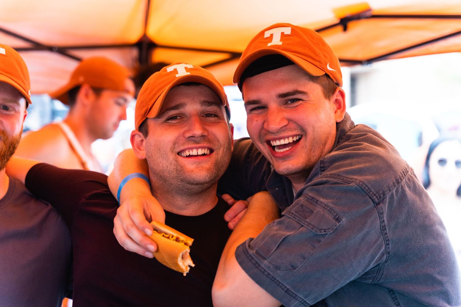Friends laughing together under orange tent at outdoor celebration.