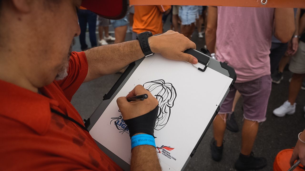 Artist sketching portrait on clipboard at outdoor event.