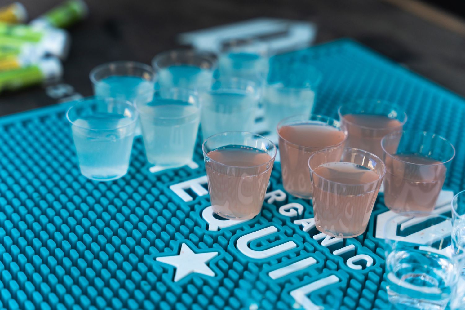 Blue and pink shot glasses arranged on a turquoise bar mat with star decoration.