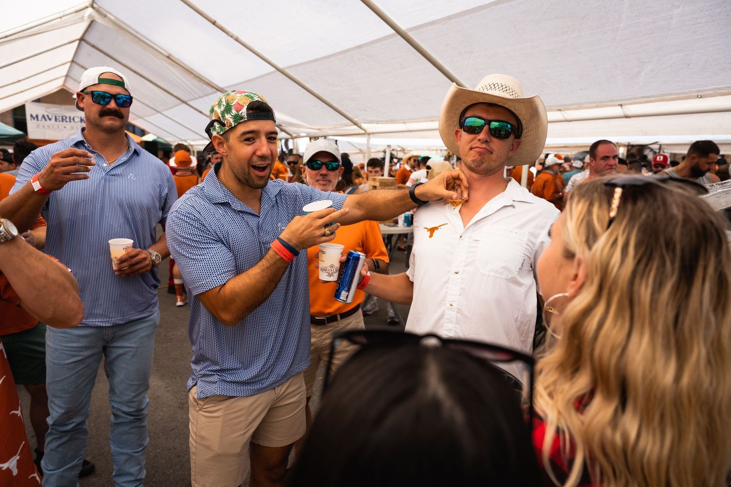 Energetic tailgating scene under a white tent with fans in sports attire.