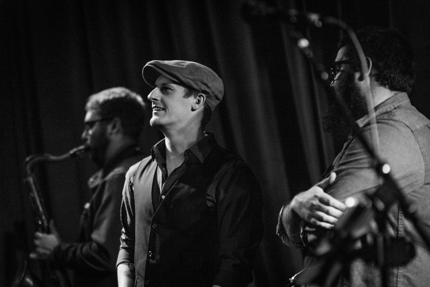 Musicians perform on stage with saxophone and other instruments in black and white lighting.