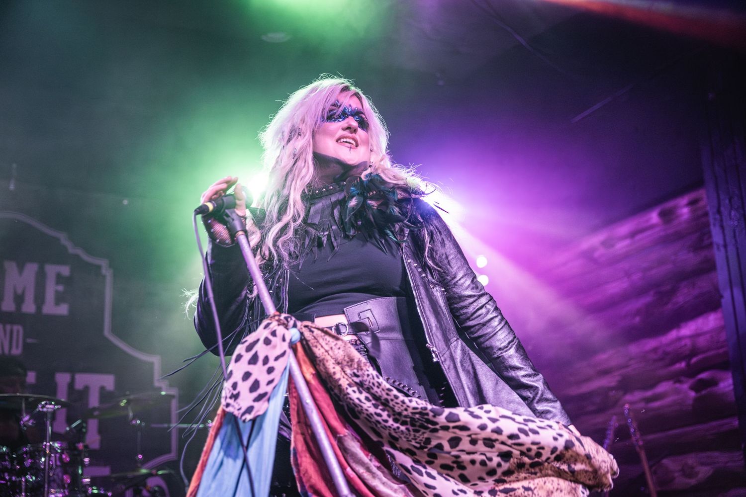 Rock performer in leather jacket with animal print fabric under colorful stage lights.