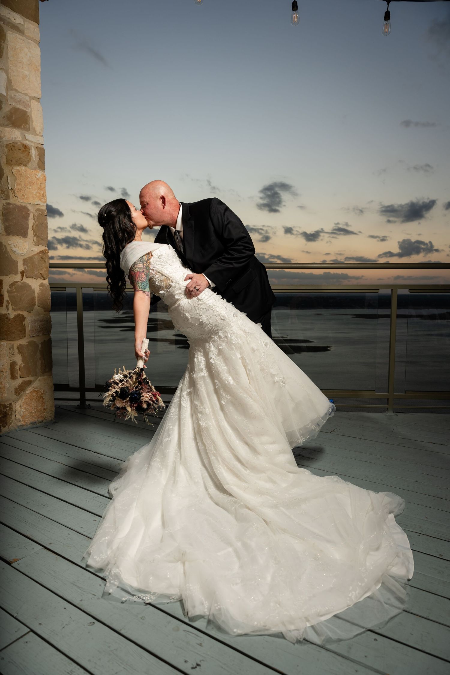 Dramatic dip pose wedding photo on balcony at sunset.