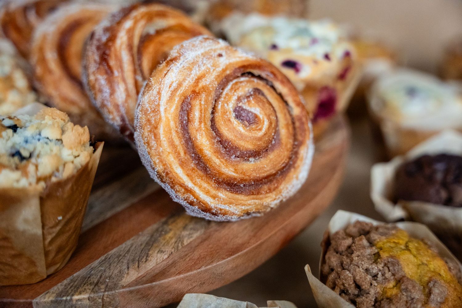 Fresh baked cinnamon rolls with swirls of cinnamon and sugar on a wooden serving board.