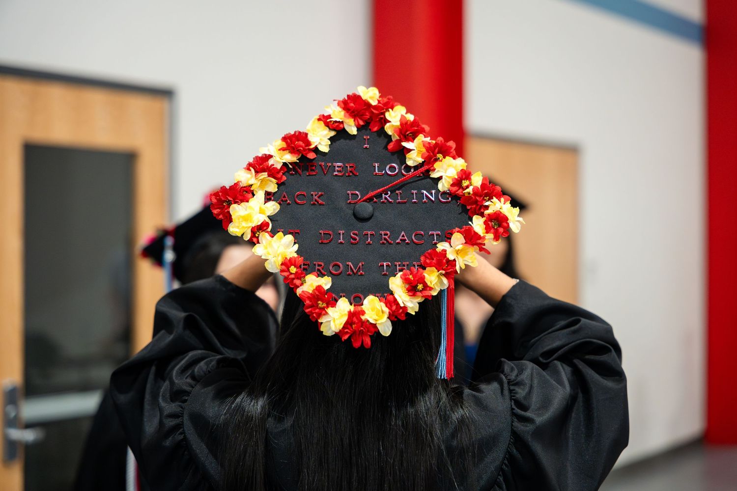 Graduation cap decorated with red and yellow flowers against light background.