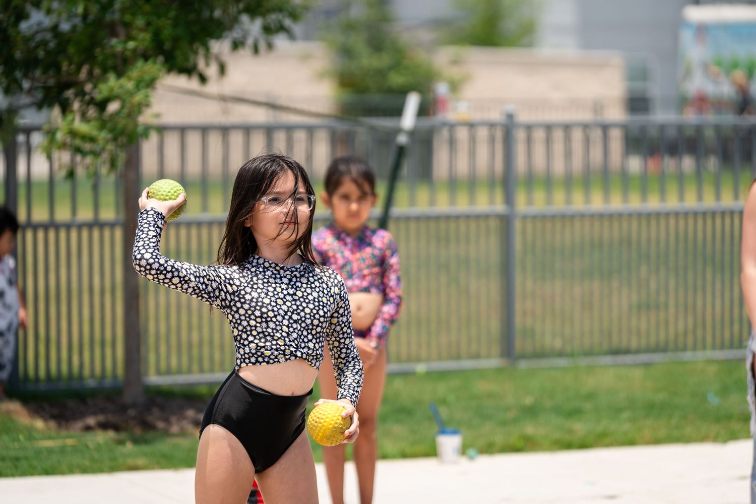 People playing an outdoor game with yellow balls in a fenced area.