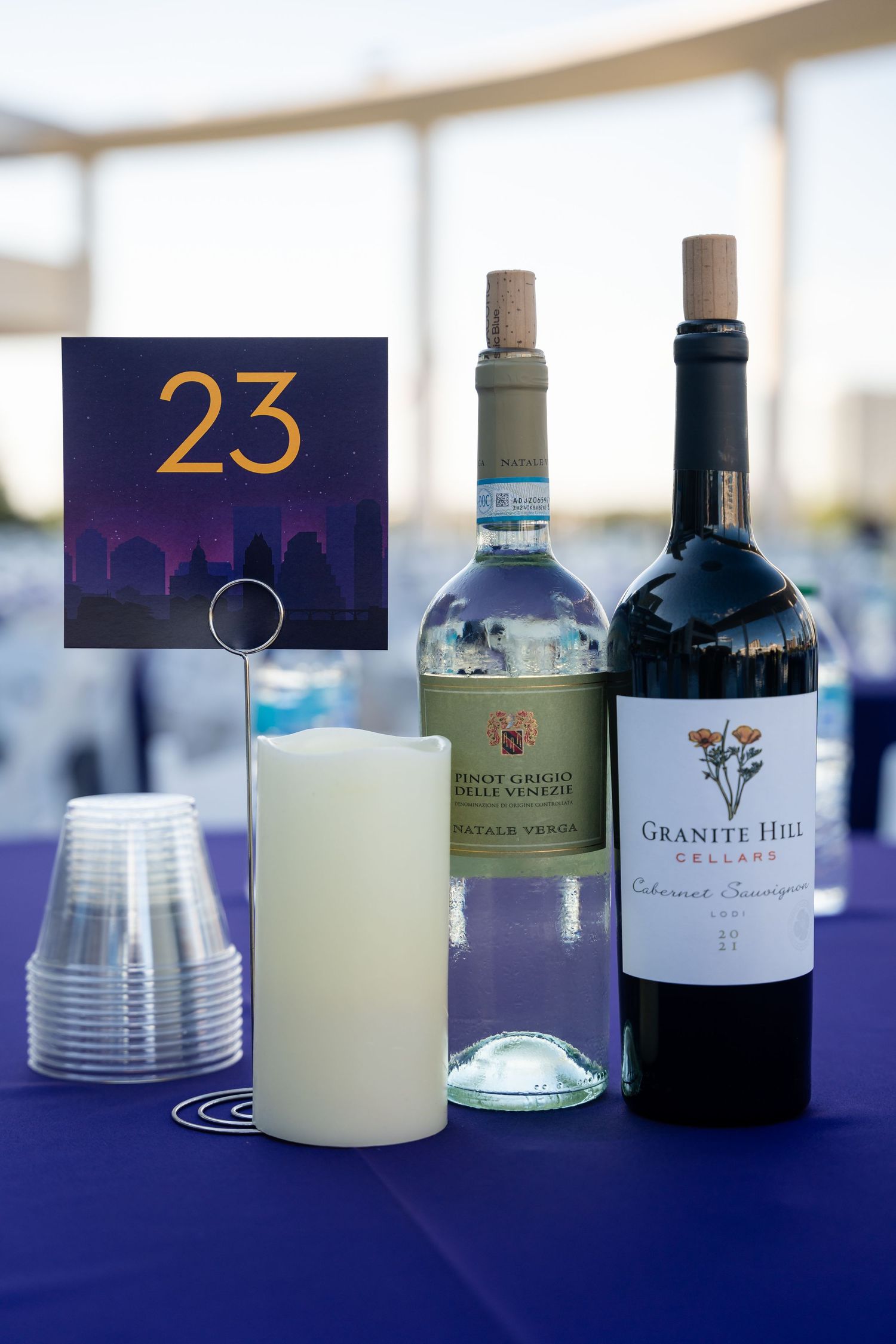 Table setting with wine bottles and table number 23 on blue tablecloth.