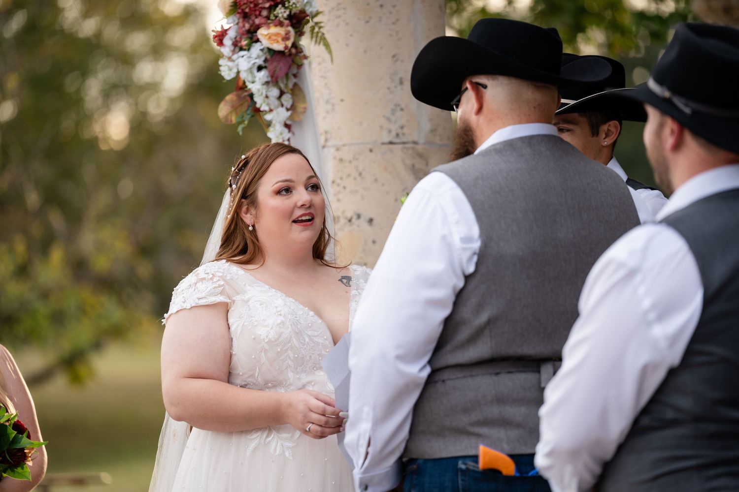 A joyful moment during a western-themed wedding ceremony near stone columns with floral decorations.
