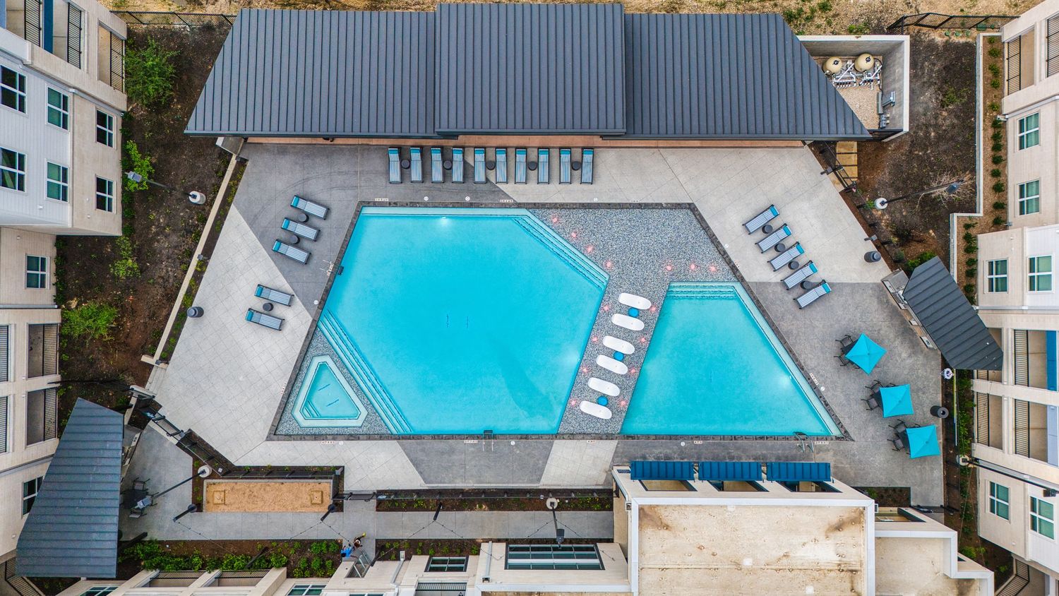 Overhead drone shot of geometric swimming pool with lounge chairs at luxury apartment building.