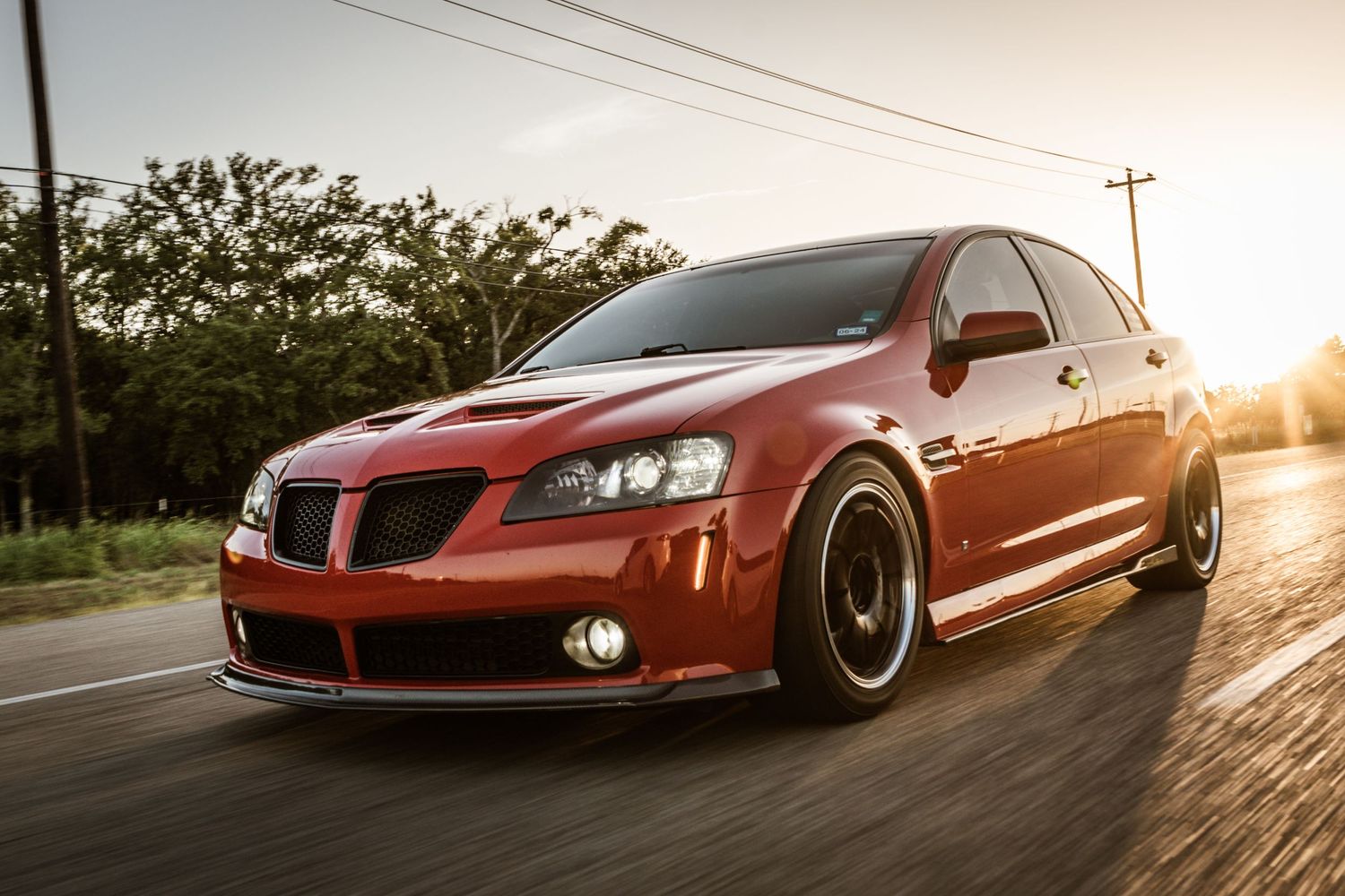Modified red Pontiac G8 GT with black wheels racing down street at sunset.