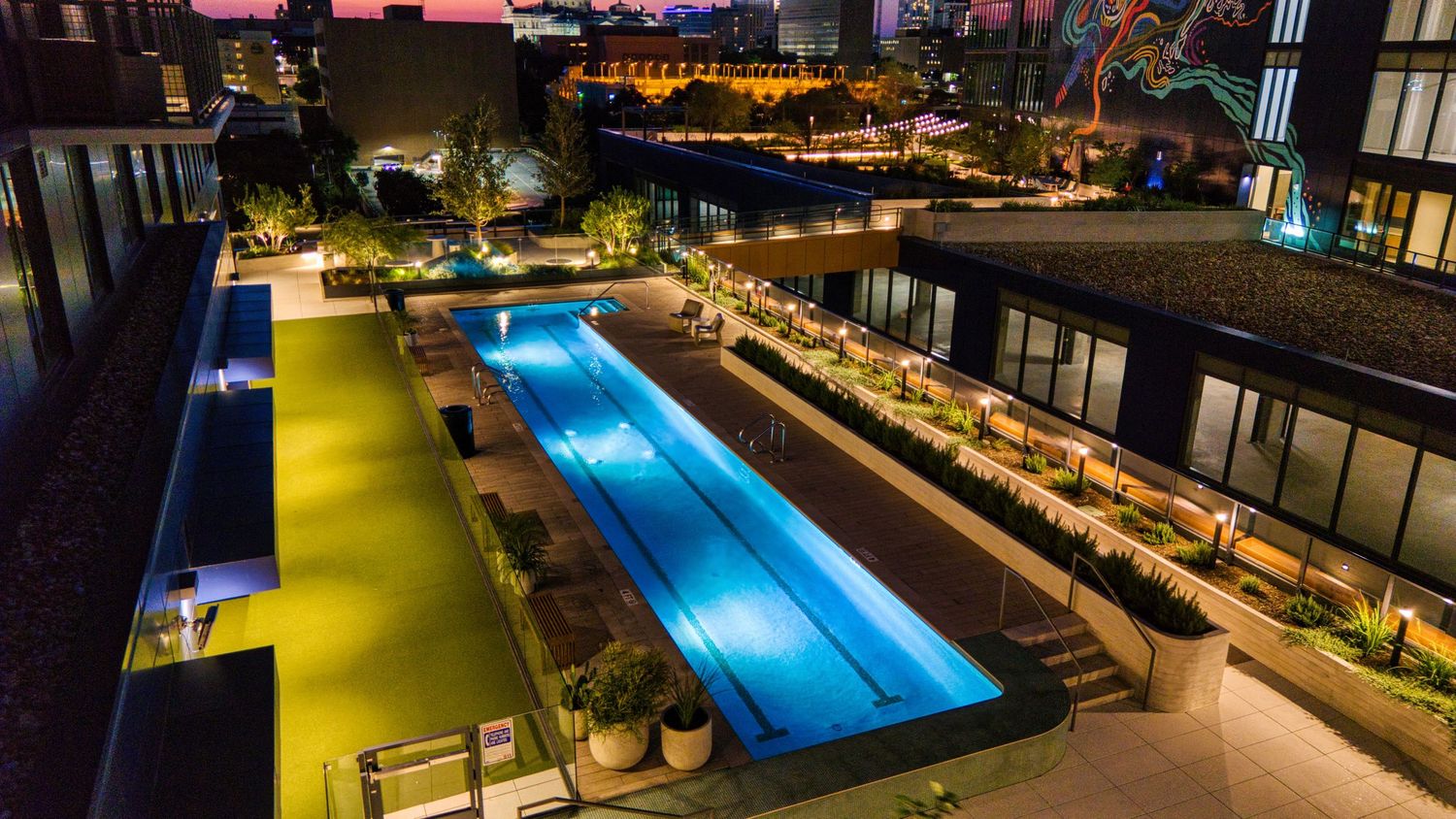 Nighttime aerial view of illuminated rooftop lap pool with adjacent lounge seating areas.