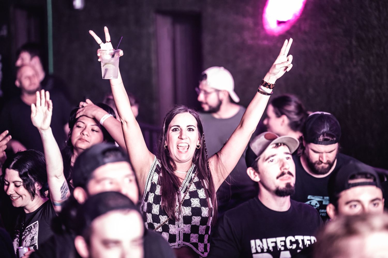 Energetic concert crowd with raised hands during nighttime music performance under purple lighting.