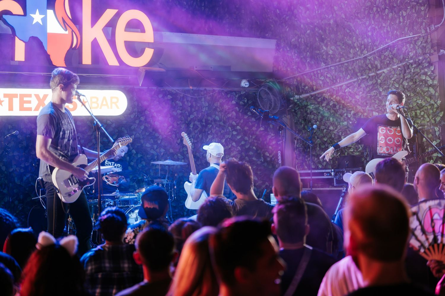 Band performing under purple lighting at a live music venue with crowd in foreground.