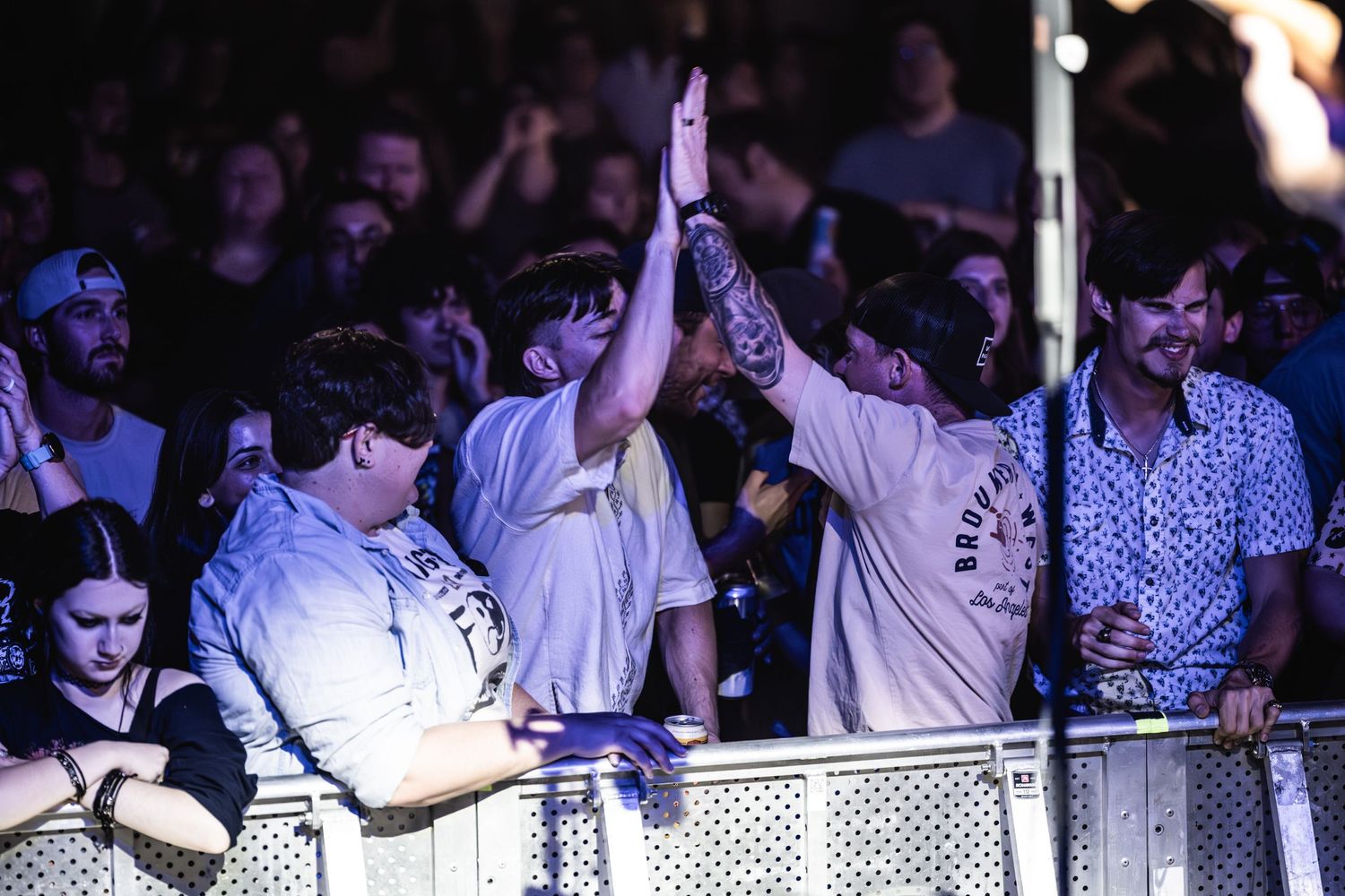 Concert attendees raise their hands in excitement while standing behind venue barriers.