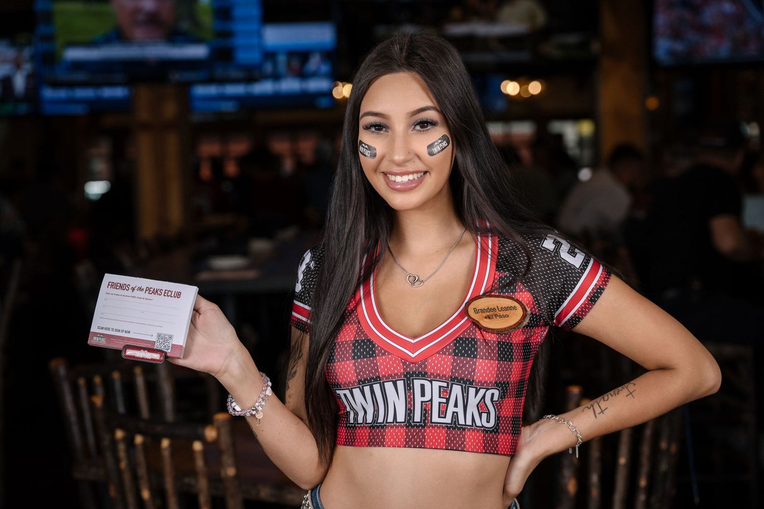 Twin Peaks restaurant staff member poses with business card in branded uniform top.
