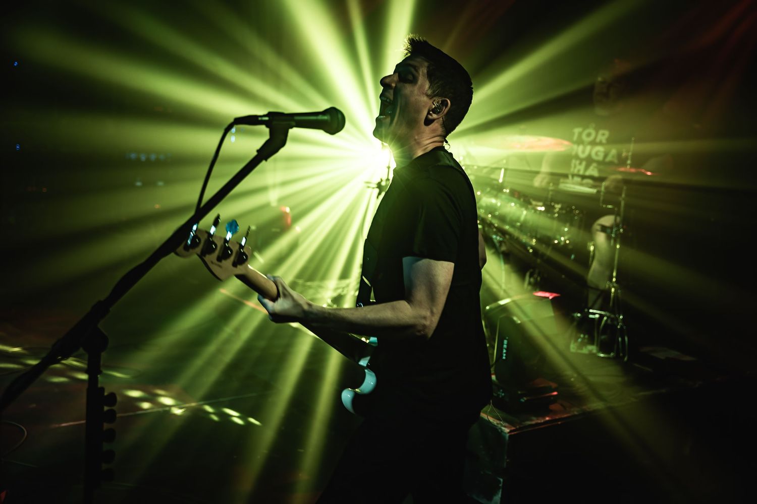Musician singing and playing guitar with dramatic green backlighting on stage.