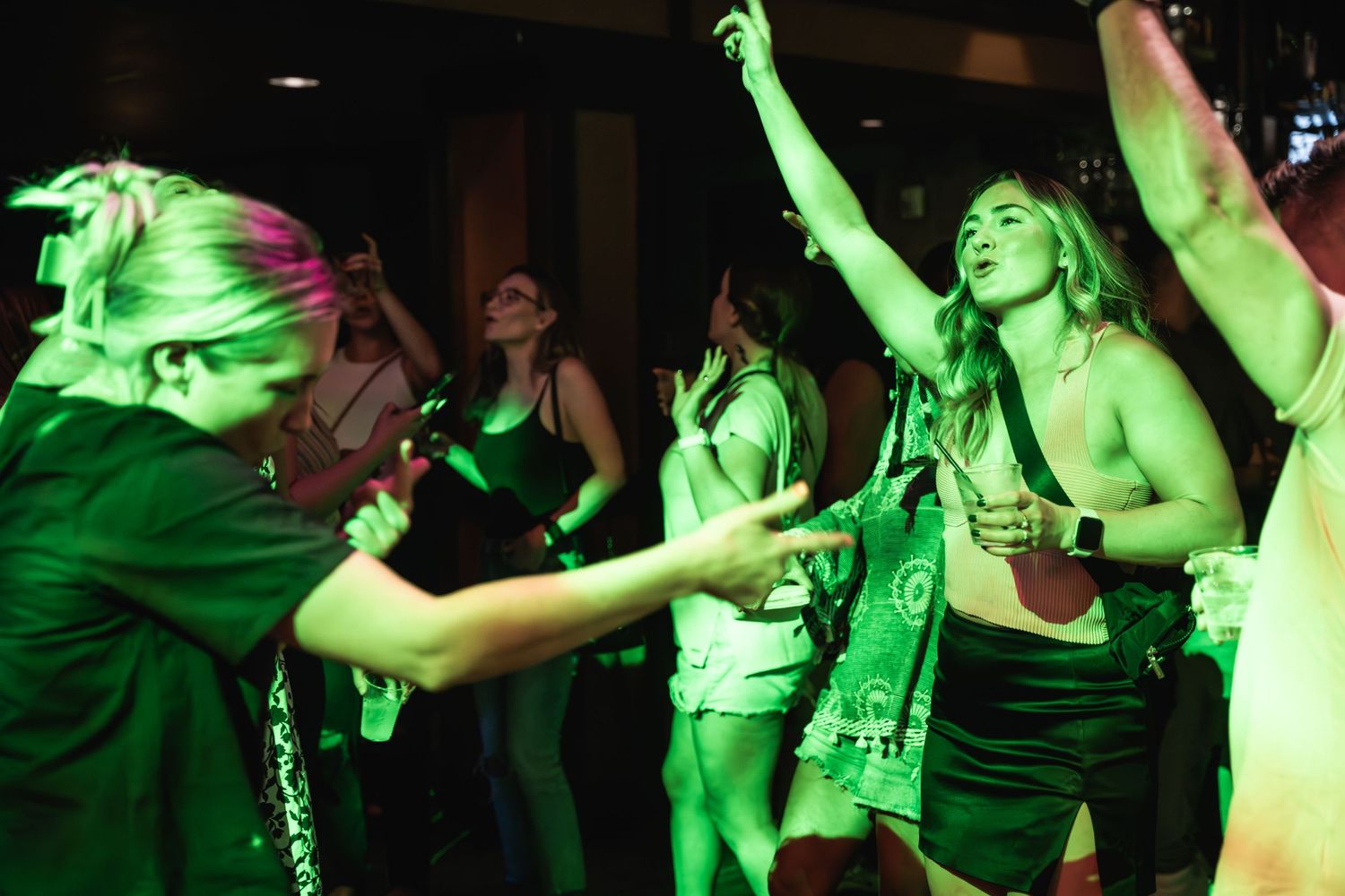 Concert attendees dance enthusiastically under green venue lighting.