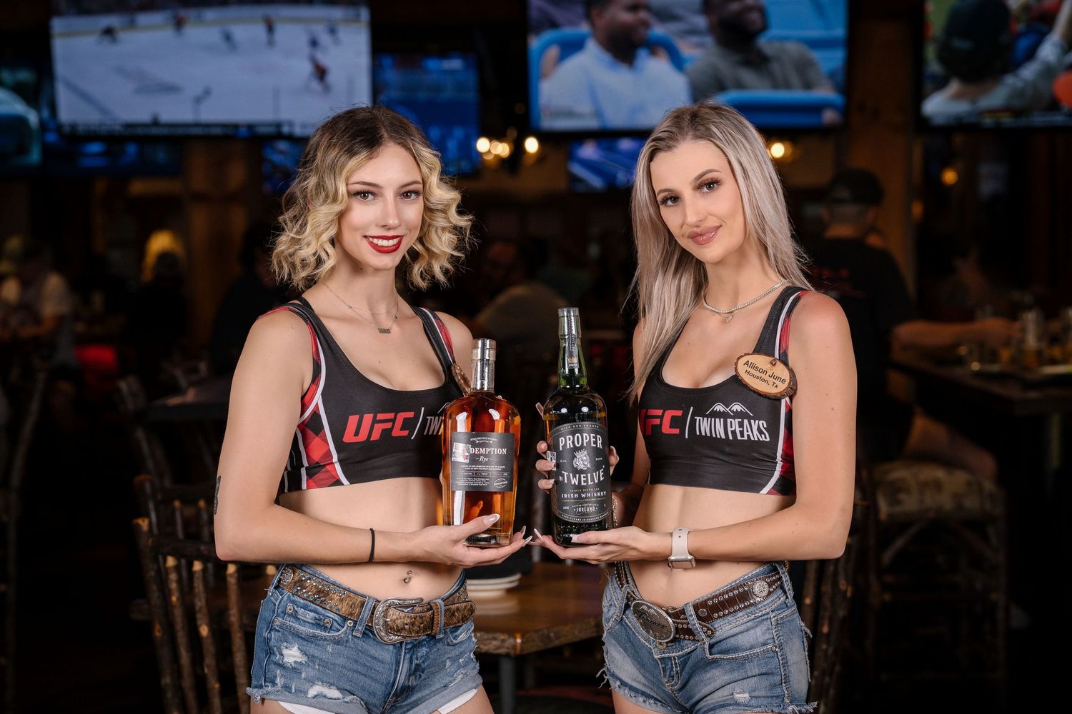 Two UFC brand ambassadors holding liquor bottles in sports bar setting.