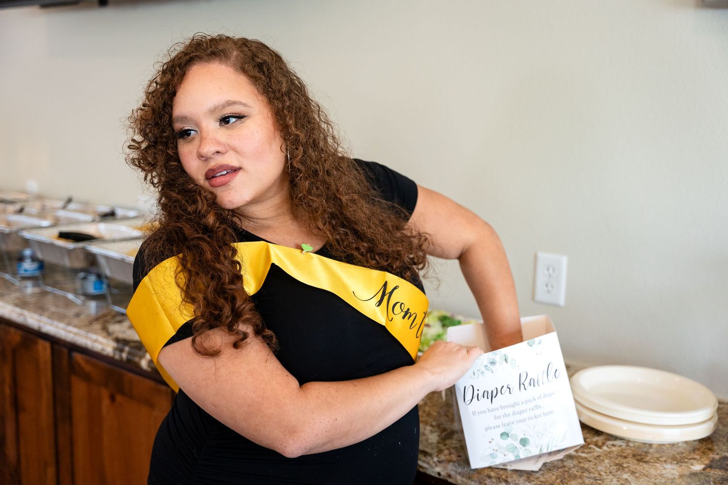 A person poses confidently wearing a yellow sash at a baby shower event.