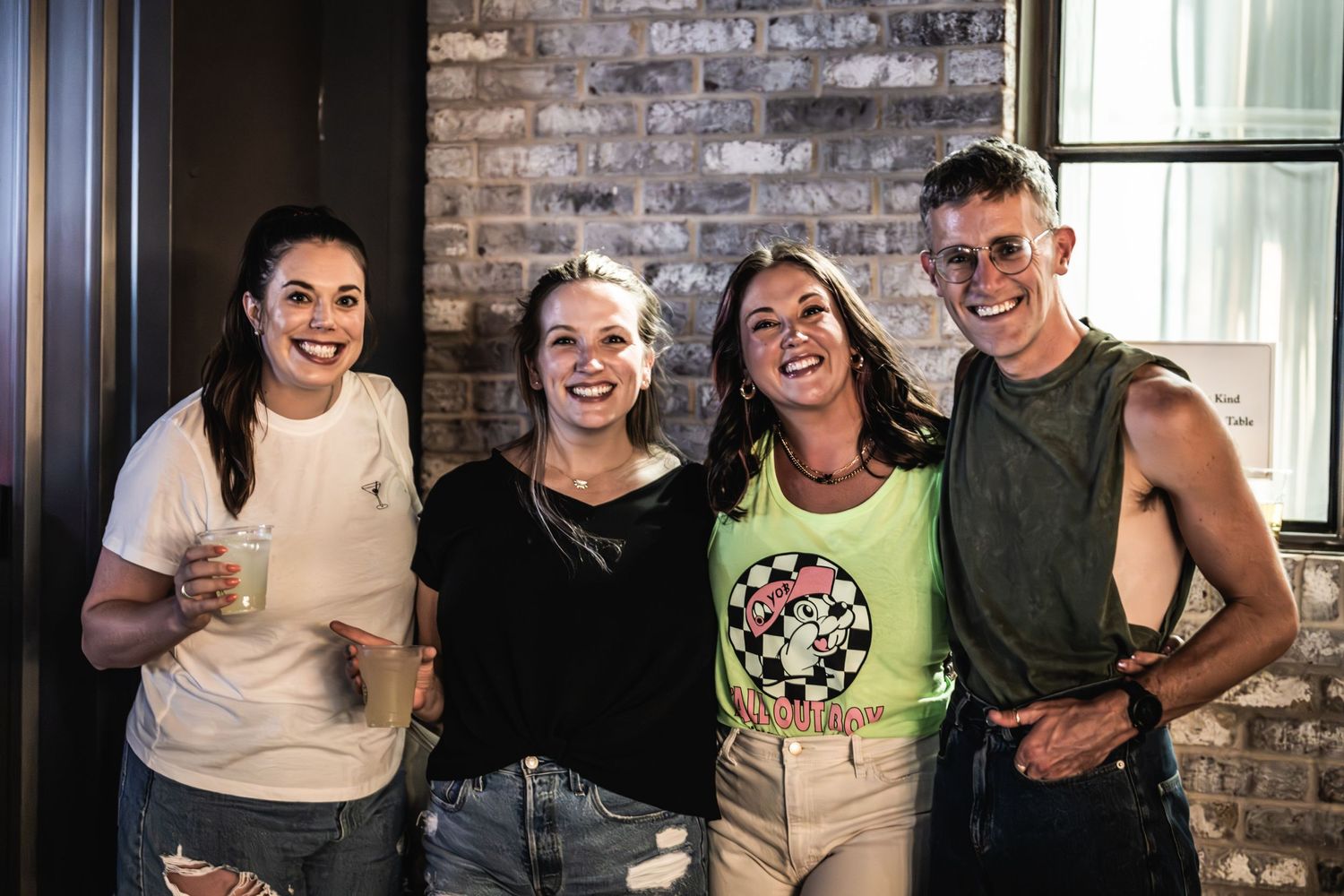 Group poses together against brick wall at music venue.