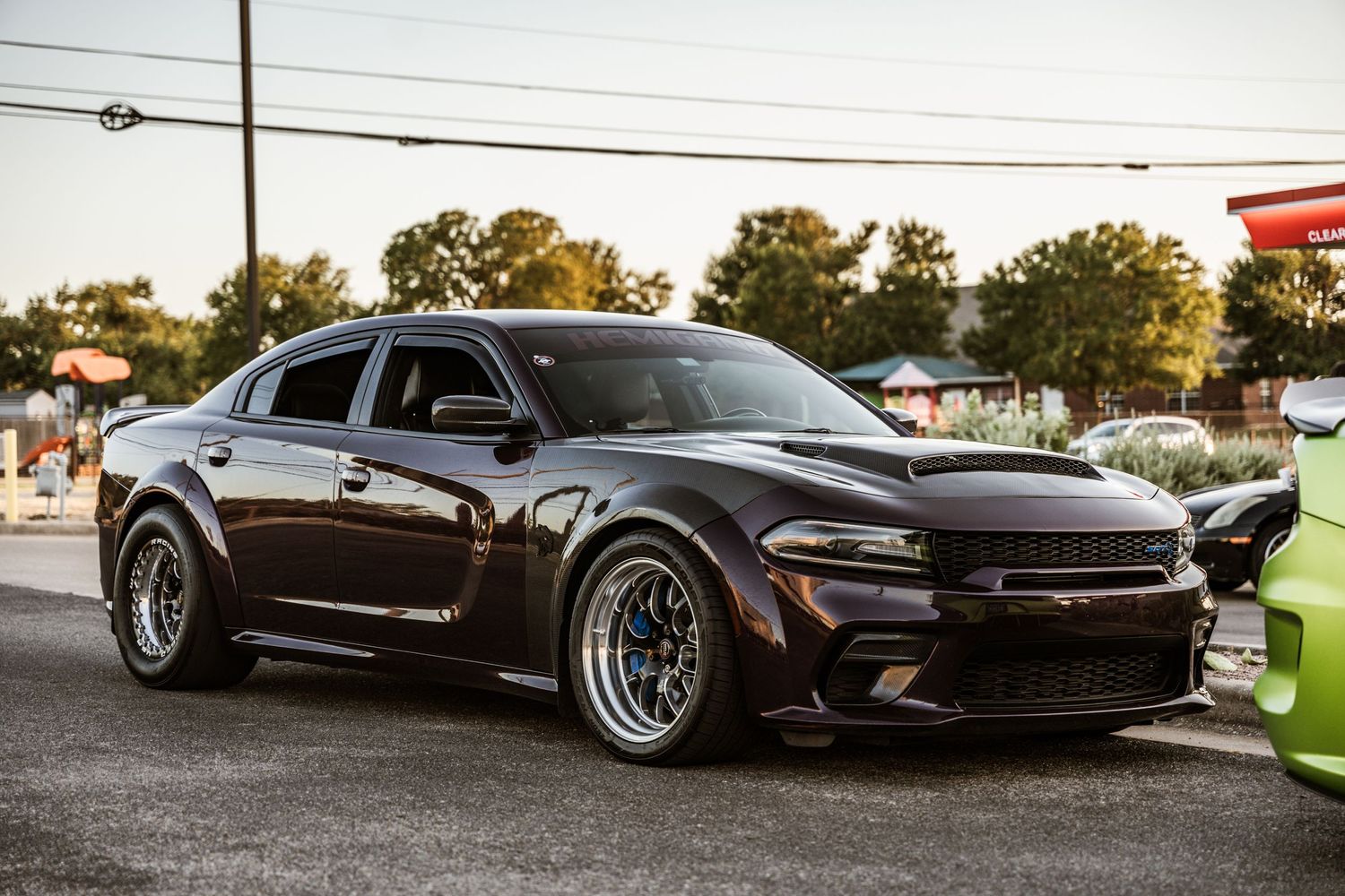 Modified black Dodge Charger with custom wheels parked in a lot at dusk.