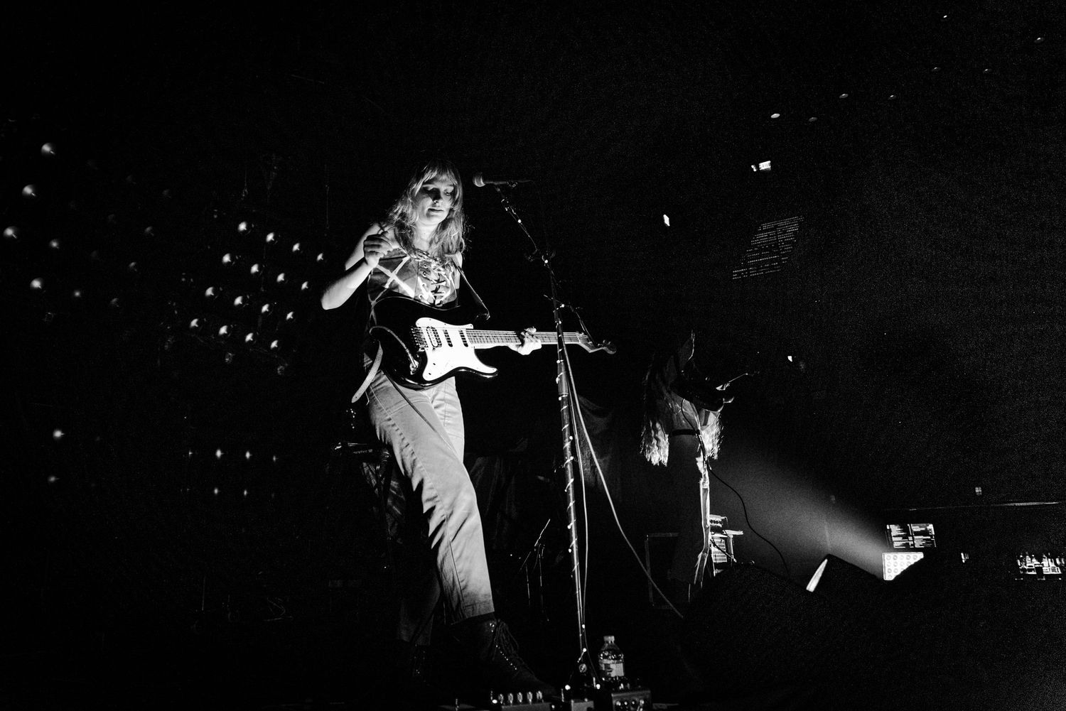 Black and white concert photo showing guitarist performing under dramatic spotlights.