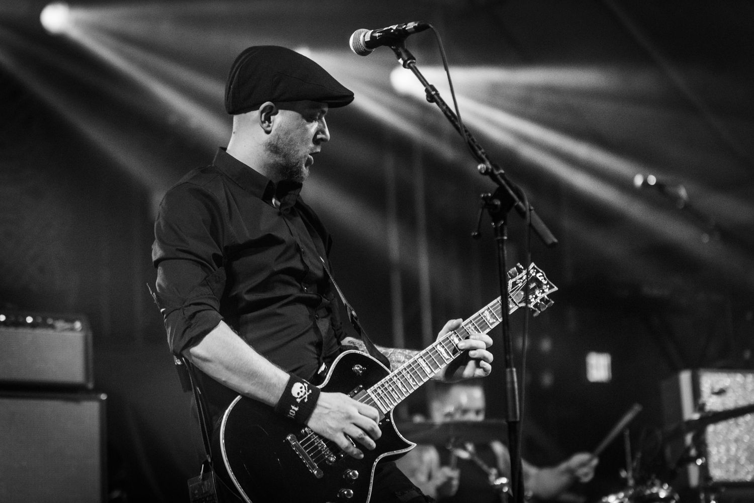 Black and white concert photo of guitarist performing under dramatic spotlight beams.