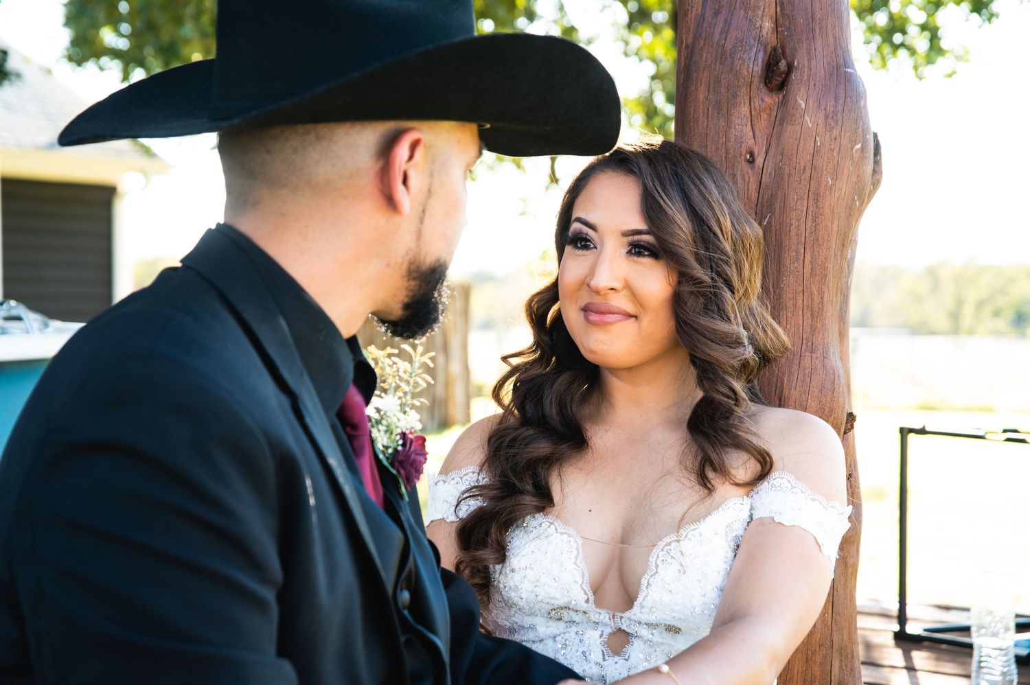 Close up of couple in western wedding attire sharing tender moment under wooden beam.