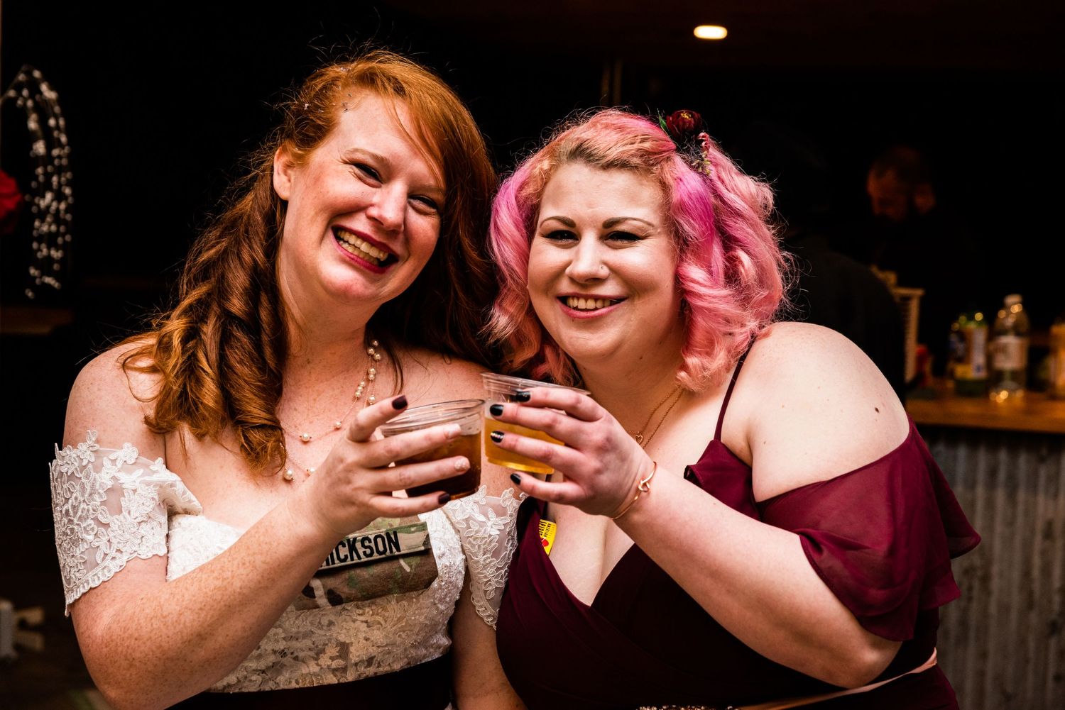 Wedding celebration with guests laughing and sharing drinks in burgundy and white attire.