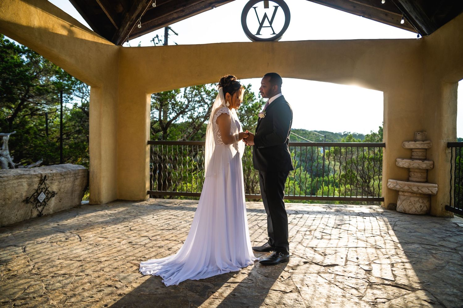Wedding ceremony takes place under a rustic pavilion with stone columns and scenic backdrop.