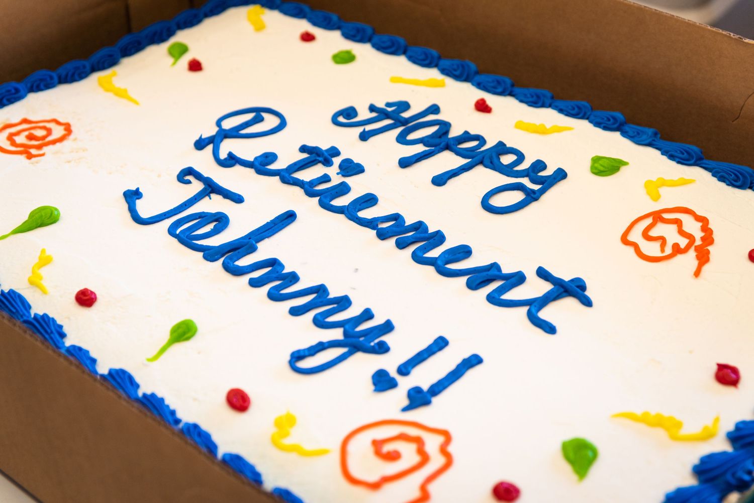 Celebration cake with blue frosted text and colorful decorative details on white icing.