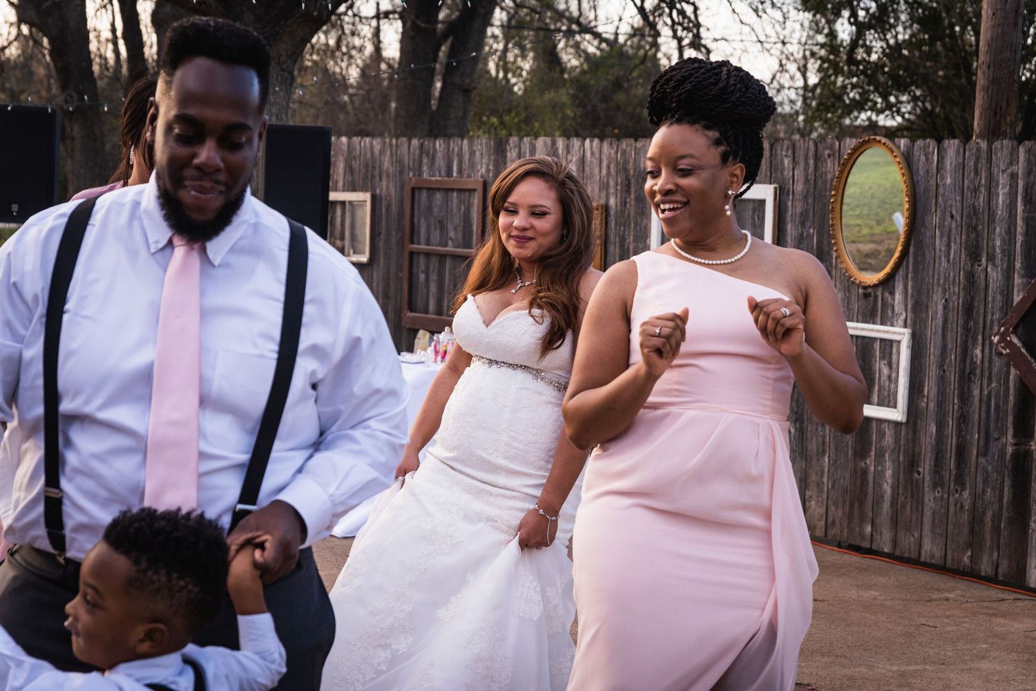 Wedding party members enjoying a lively outdoor celebration with bridesmaids in pink dresses.