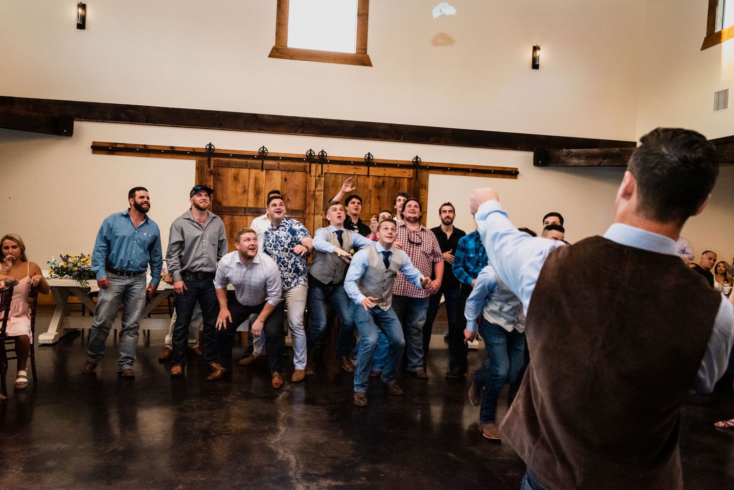 Group of wedding guests performing choreographed dance routine in rustic venue.