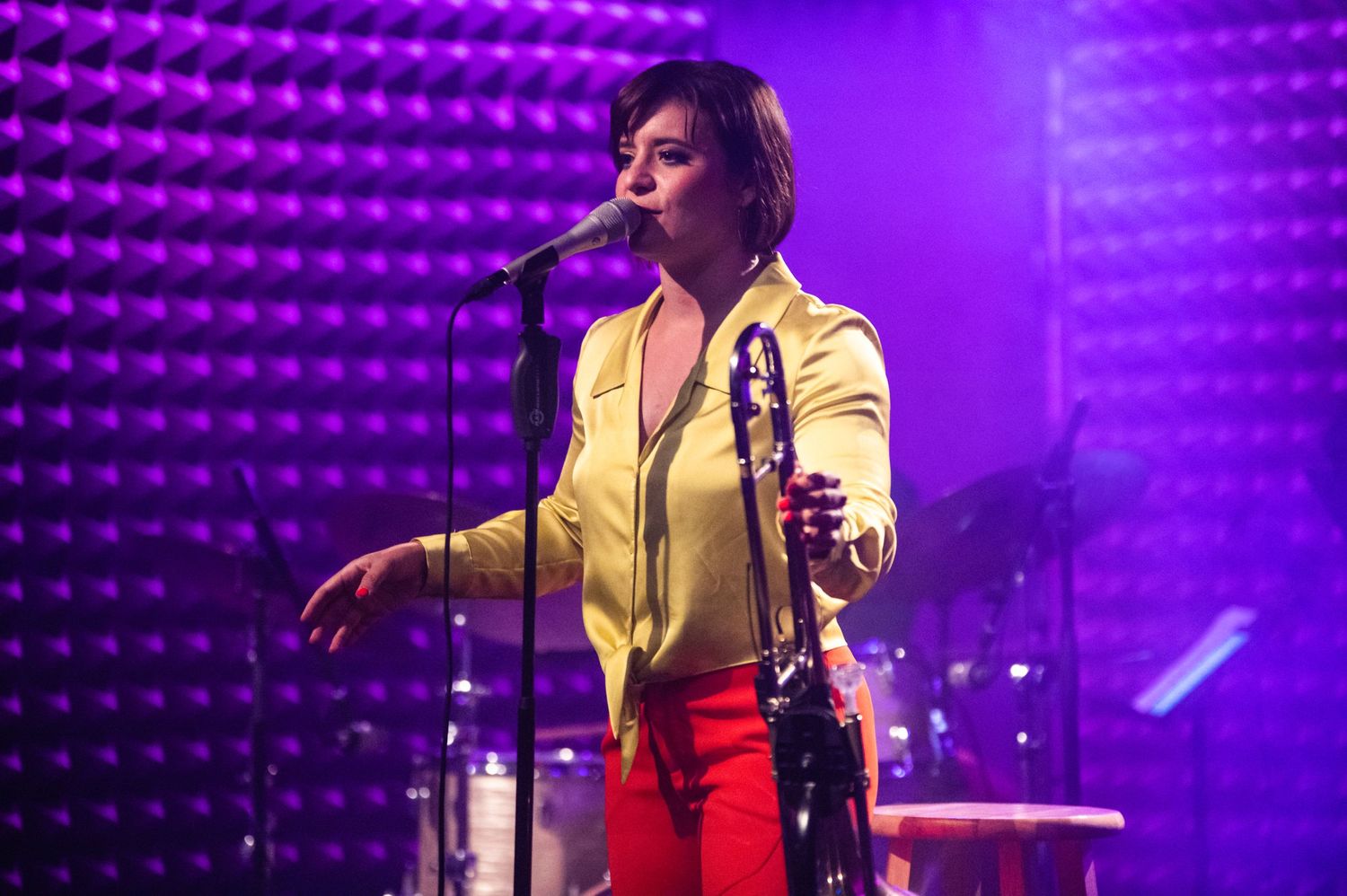 Jazz performer in yellow jacket singing on stage with purple lighting effects.