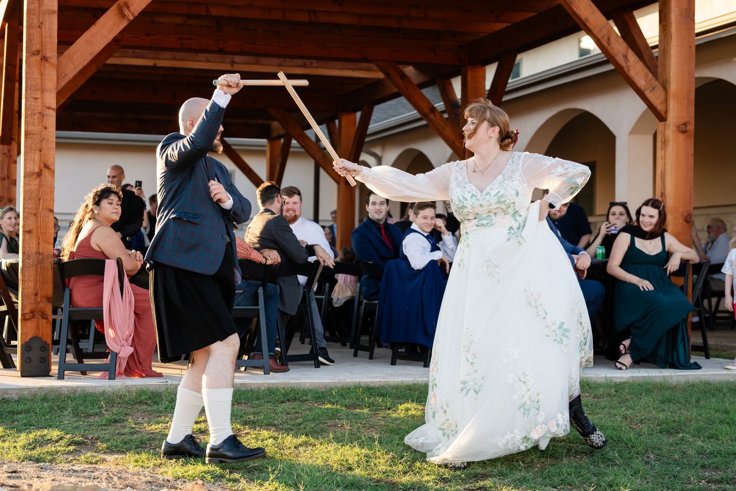 A group of wedding guests dance and celebrate together at an outdoor reception venue during sunset.
