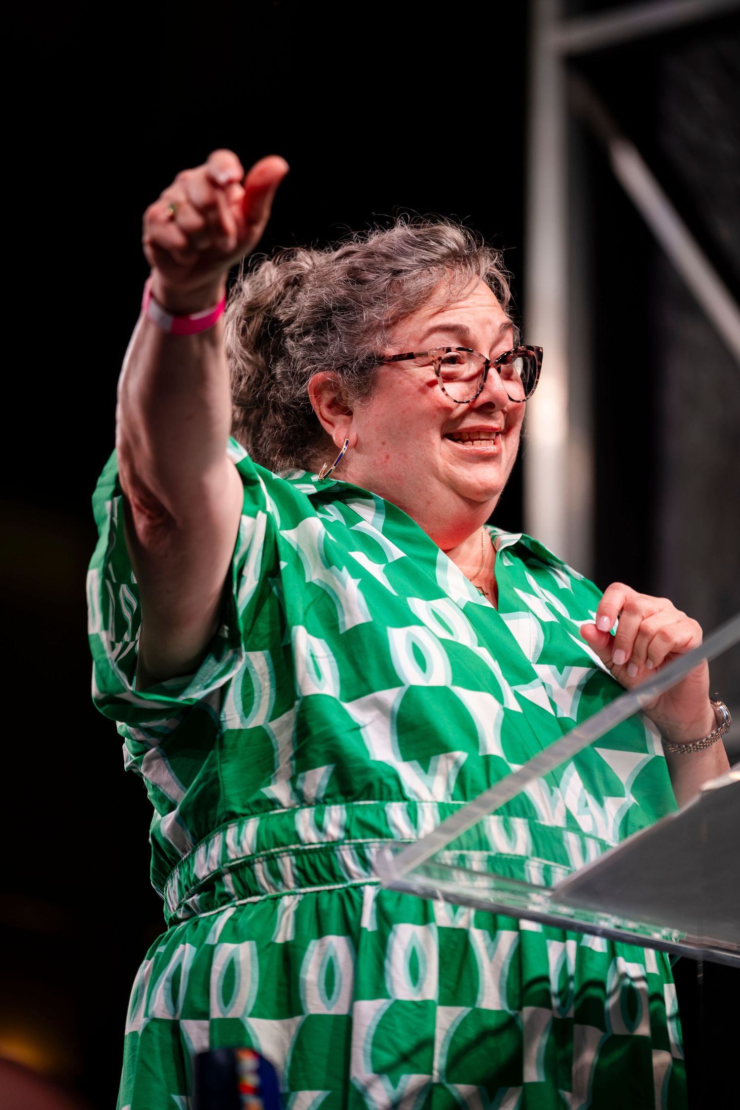 A person wearing a green and white patterned shirt raises their arms in celebration while smiling.