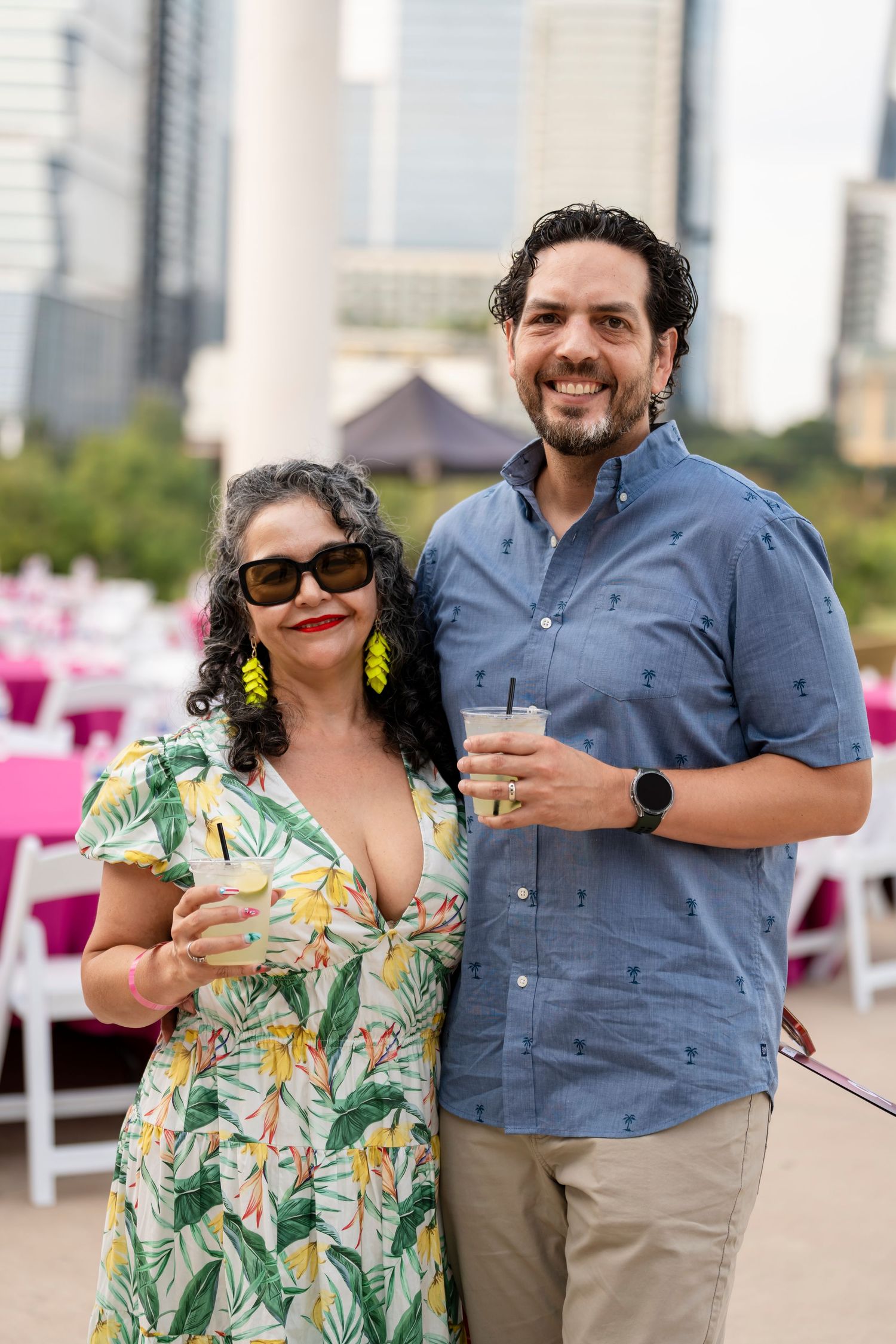 A couple enjoys drinks together at an outdoor venue with a cityscape backdrop.