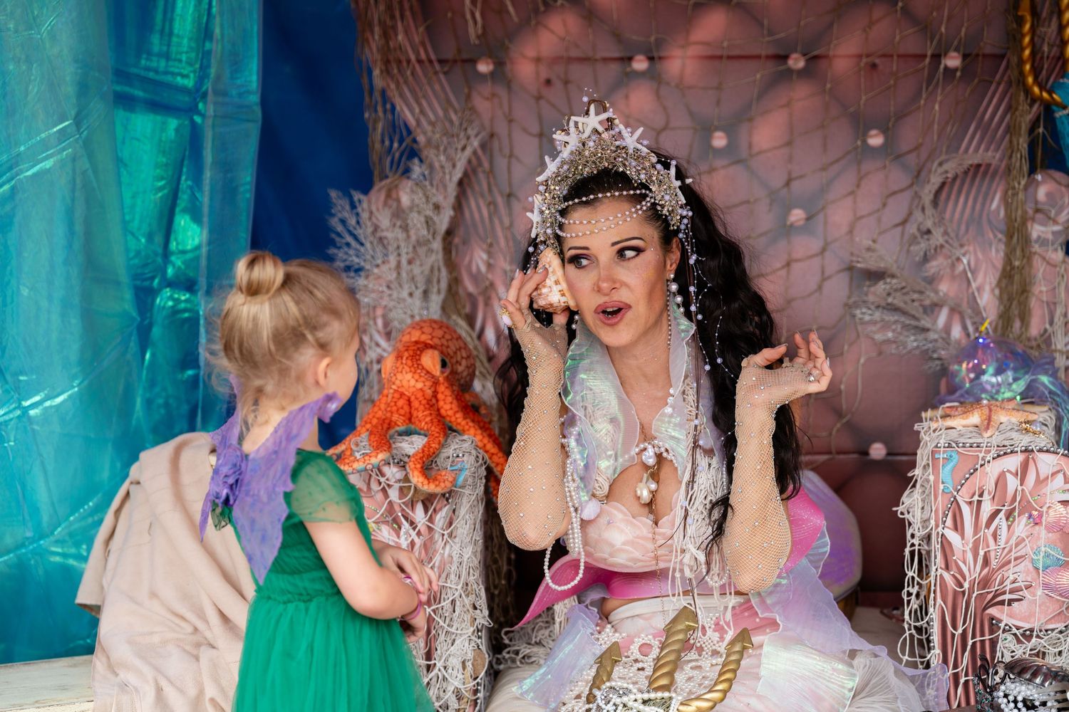 A group of people in formal attire and tiaras pose together at an elegant party with turquoise lighting and decorations.