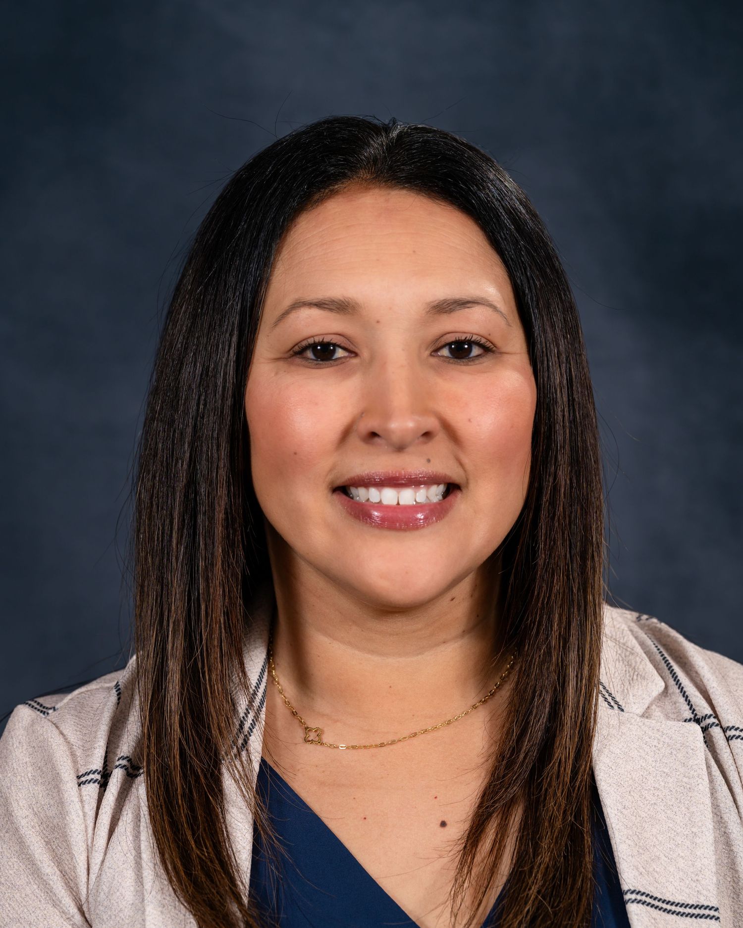 Professional headshot portrait of someone in a navy blue top and white blazer against a dark background.