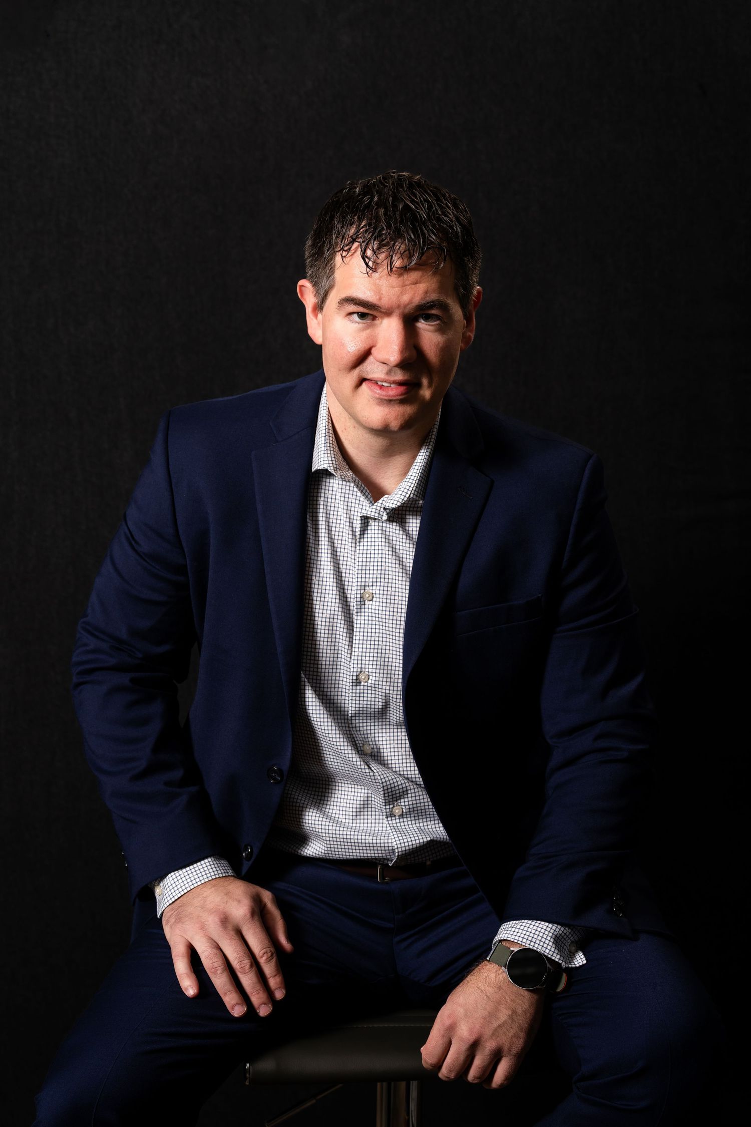 Professional studio portrait series showing person in navy suit and light dress shirt against dark background.