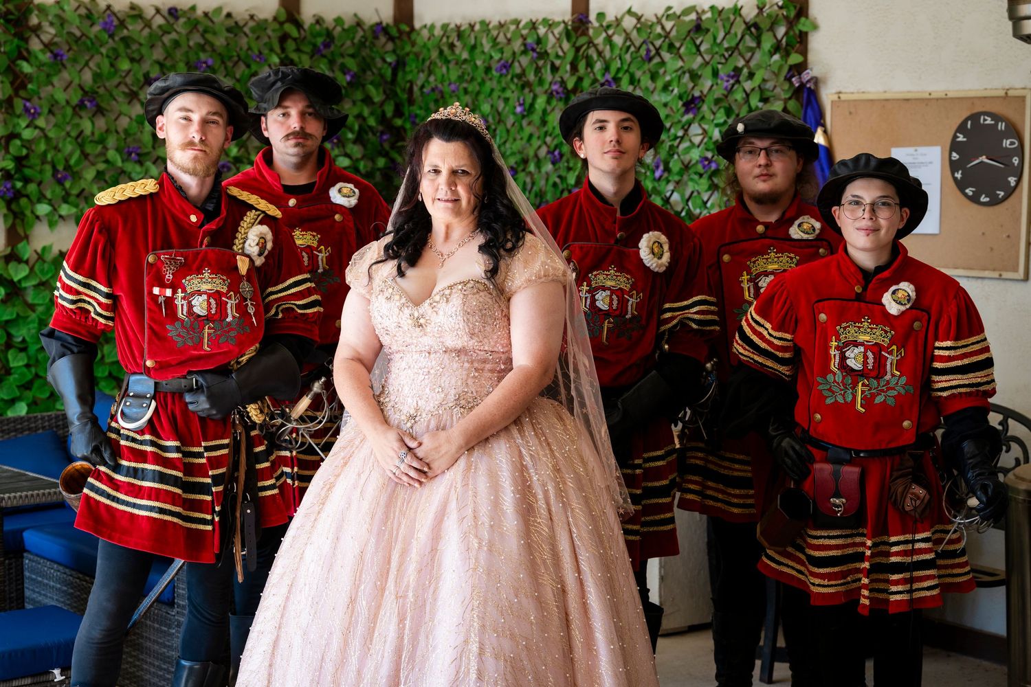 Wedding party poses in traditional red military uniforms and formal attire against a rustic backdrop.