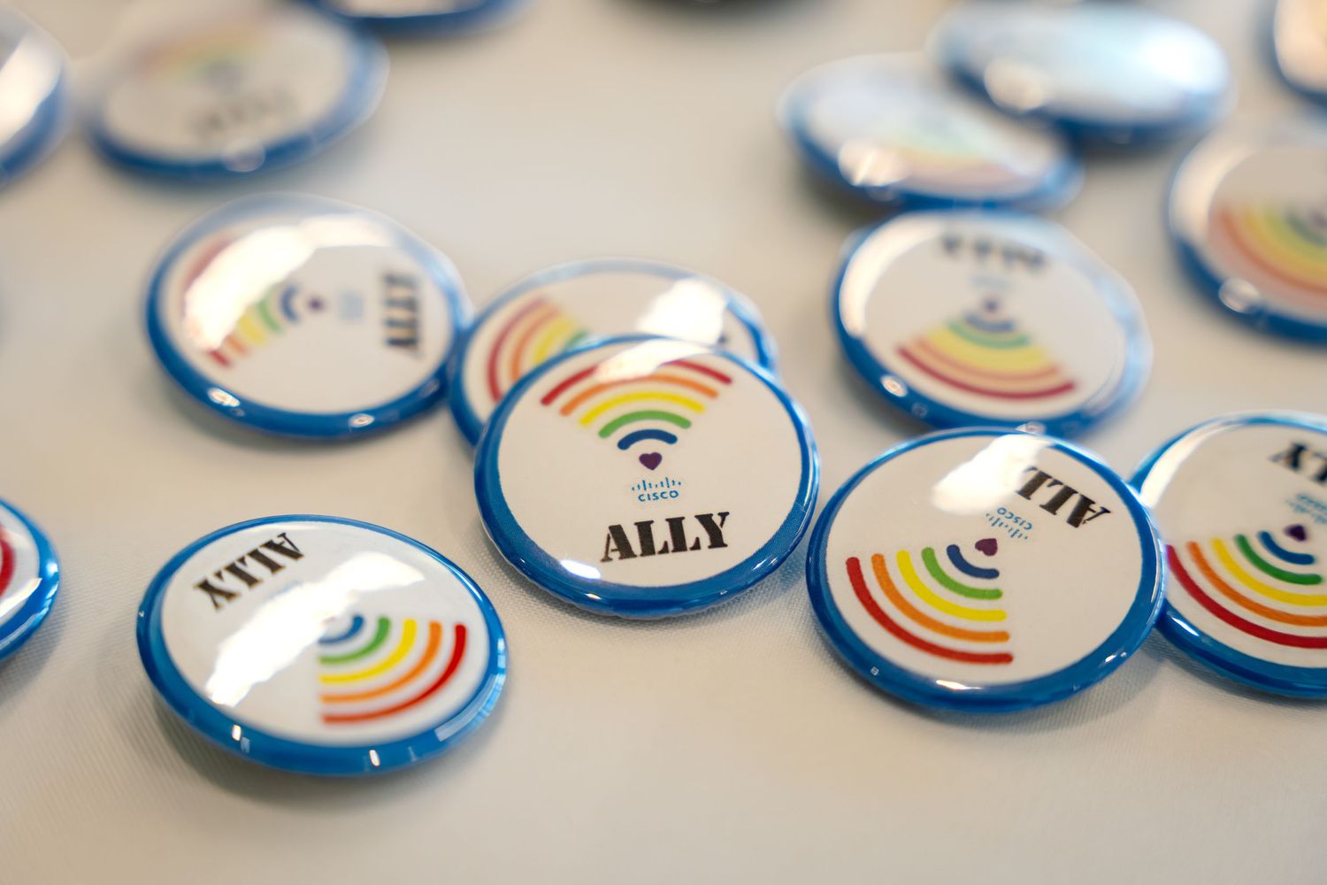 Rainbow ALLY buttons with WiFi symbol design displayed on a white surface, promoting inclusivity and support.