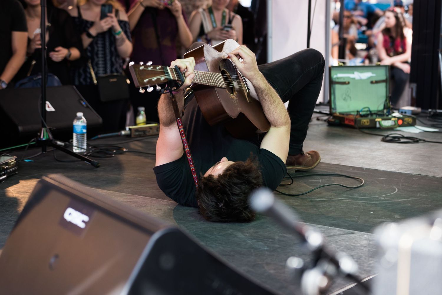 A performer lies on the ground during an energetic stage performance with dramatic lighting effects.