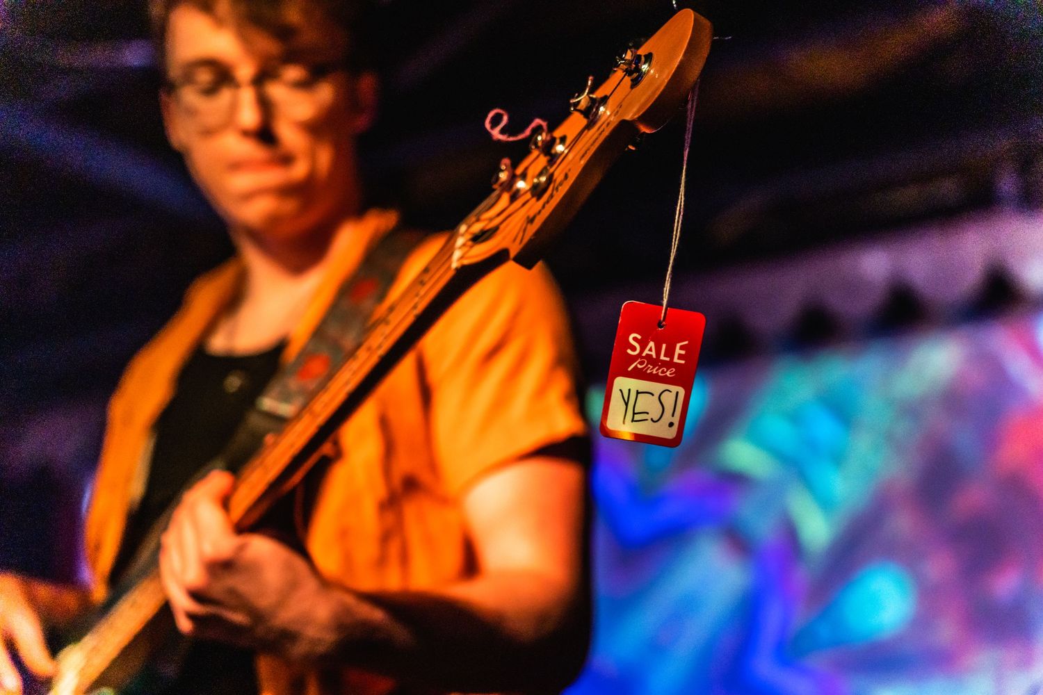 A guitarist performs on stage with colorful blue lighting in the background during a live concert performance.