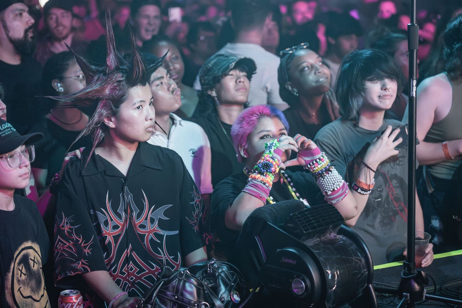A crowded concert venue with people enjoying live music in a dimly lit atmosphere with pink lighting effects.