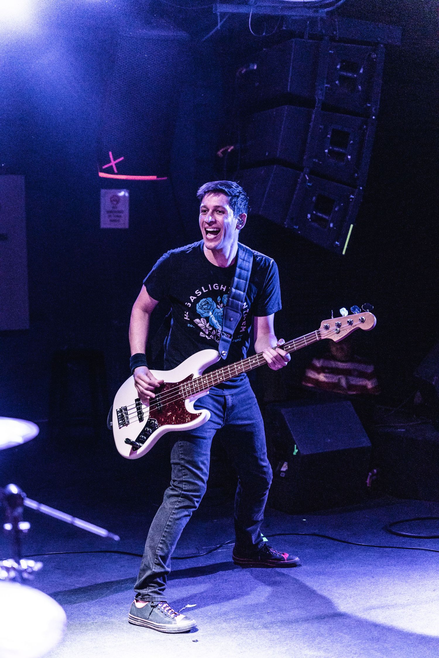 Bass player performs energetically on stage under blue lighting during a live concert performance.